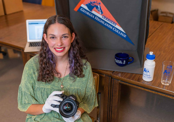 Danielle Greisemer holds camera in front of memorabilia.